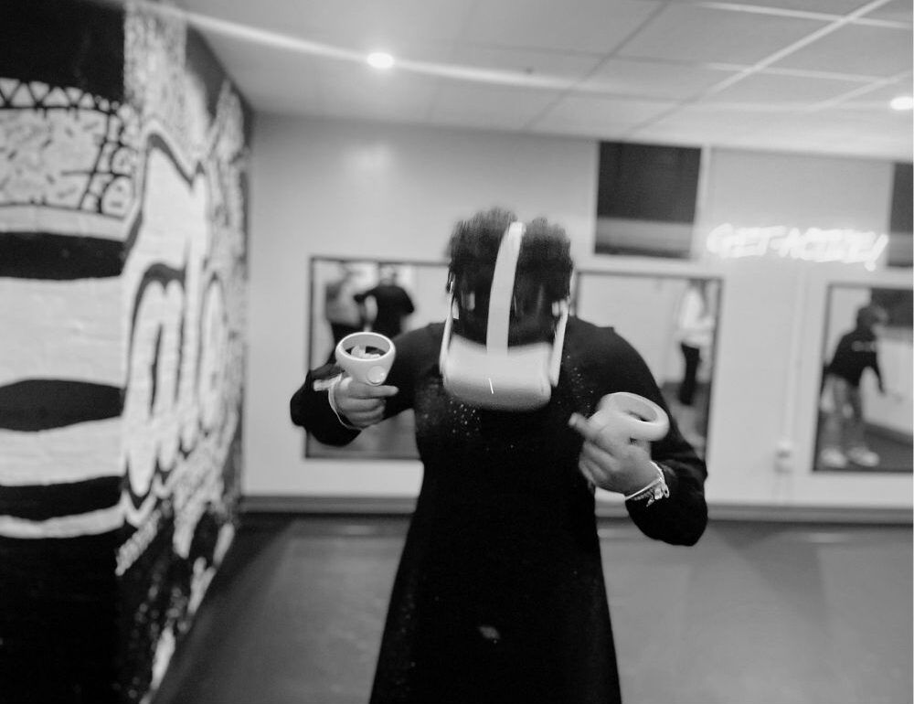 A black and white photo of a young woman using an immersive headset and handles.