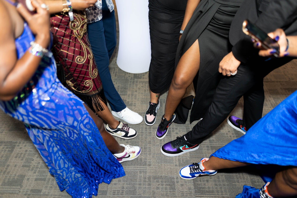 Several people in dresses and pants putting their sneaker-donning feet in a loose triangle. 