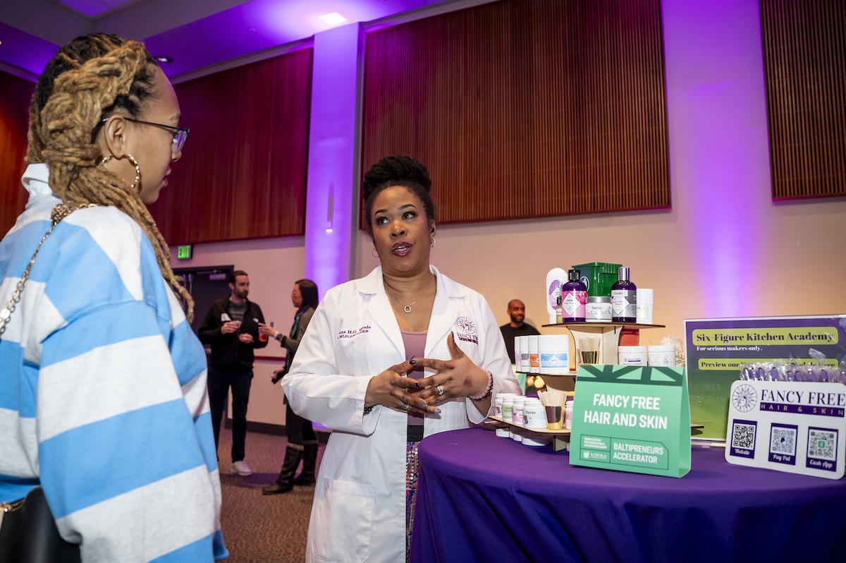 Iyonna Woods in white lab coat by her company's products on table with purple tablecloth.