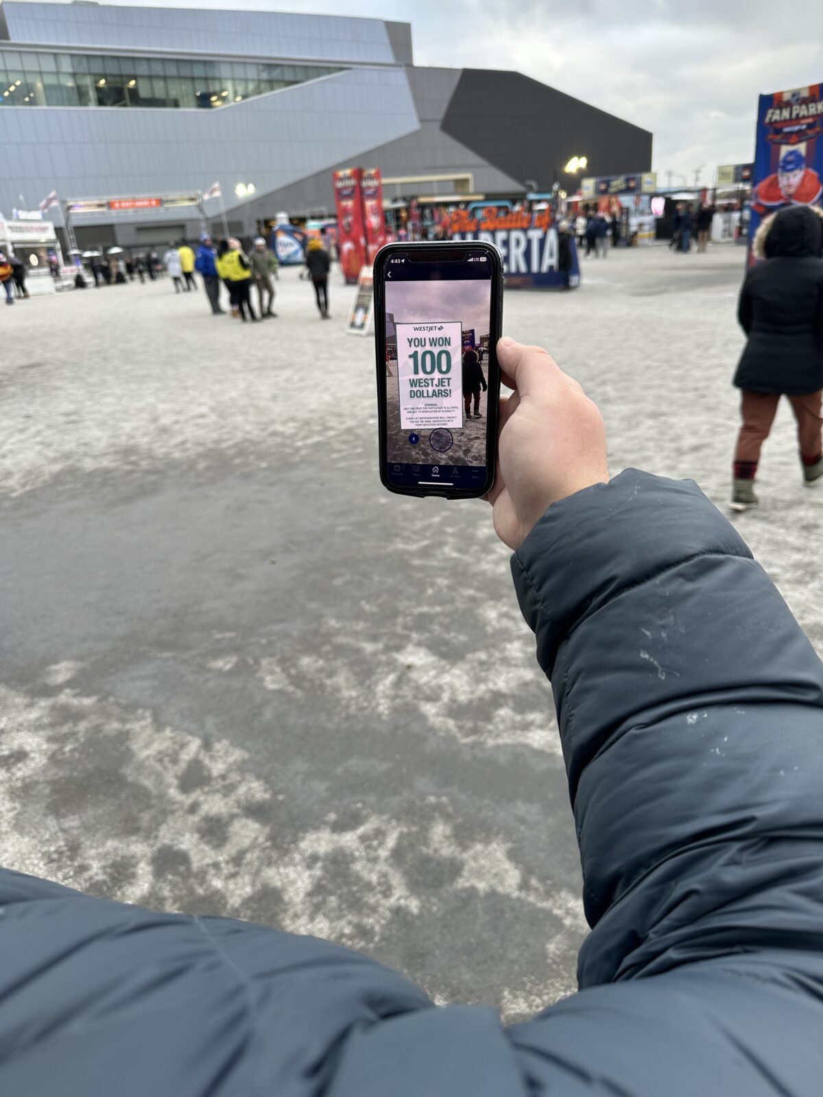 Fabric on black phone held by hand in black jacket outside grey arena.