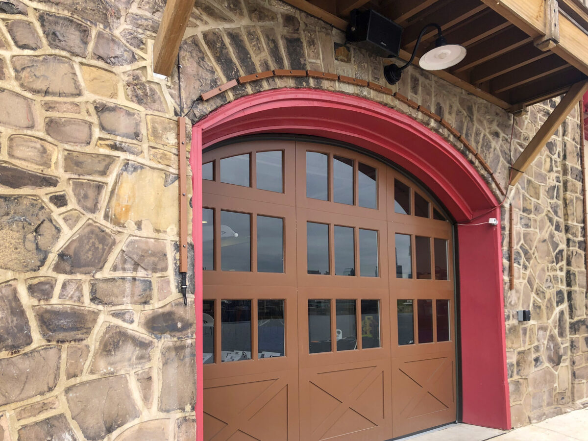 Arched wooden door with red trim set in a stone wall.