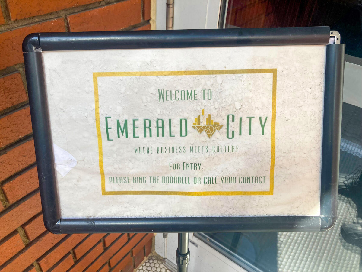 Signage titled "Welcome to Emerald City - Where Business Meets Culture" instructs visitors to ring the doorbell or call their contact for