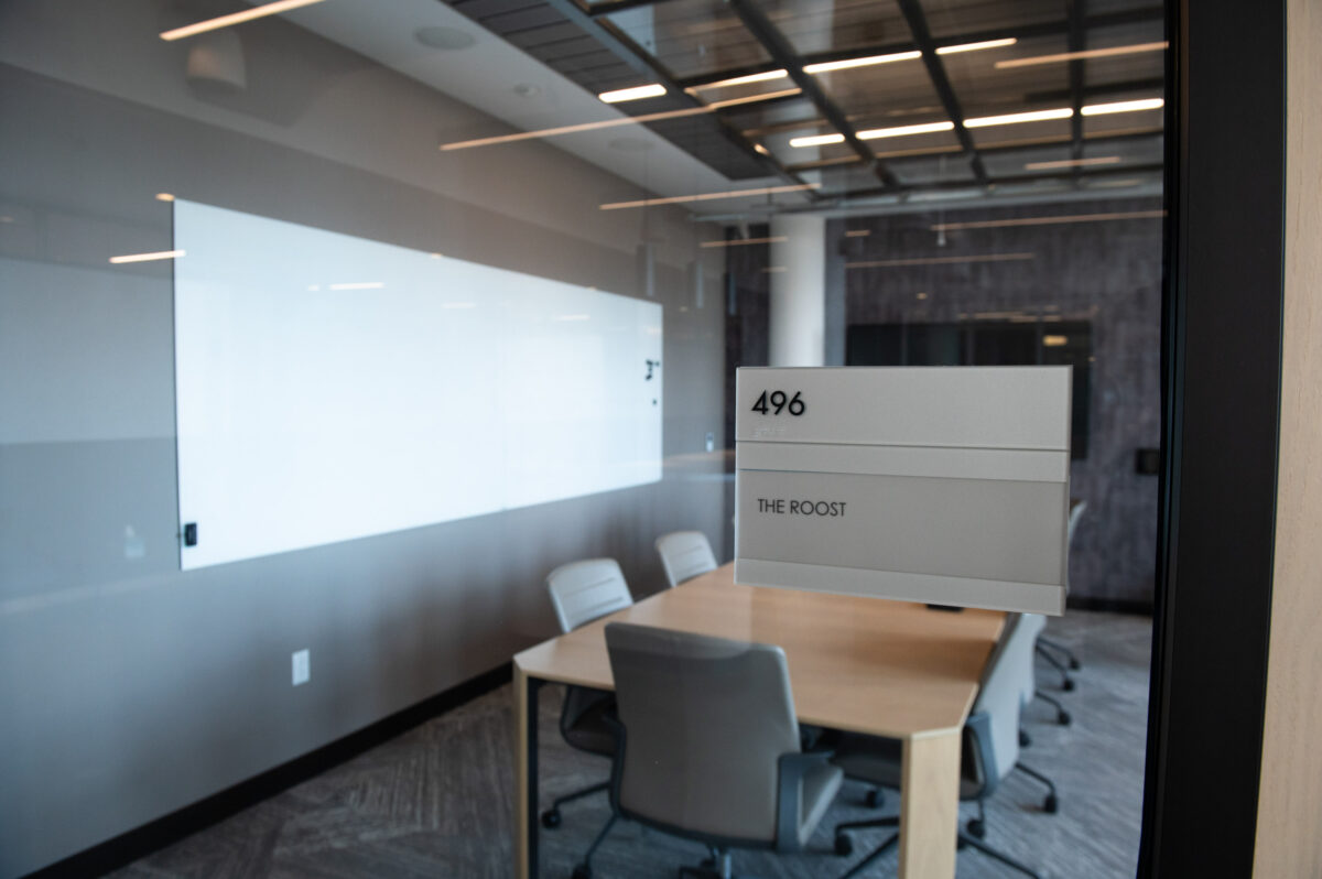 Modern conference room with a sign labeled "the roost" next to the door.