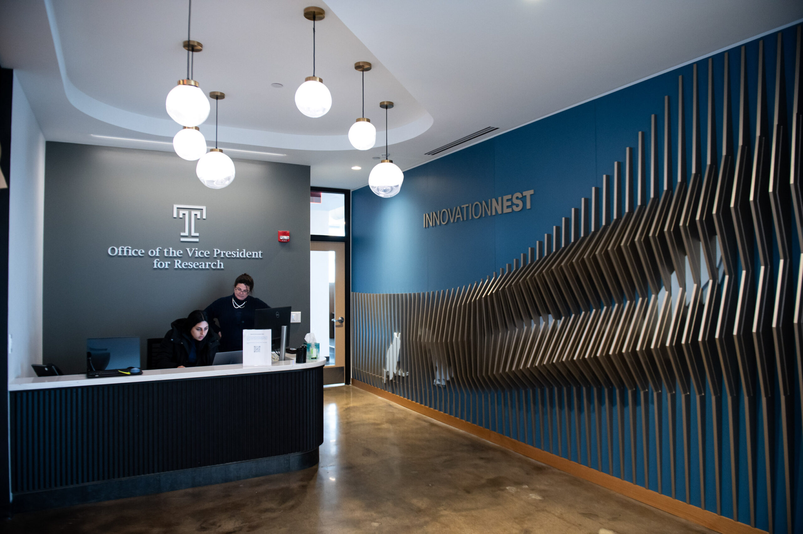 Modern office reception area with dynamic wall design and spherical pendant lights.