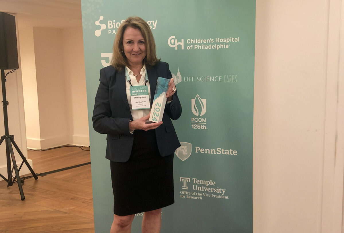 A woman in business attire proudly holding an award at a biostrategy partners event, standing before a banner with logos.