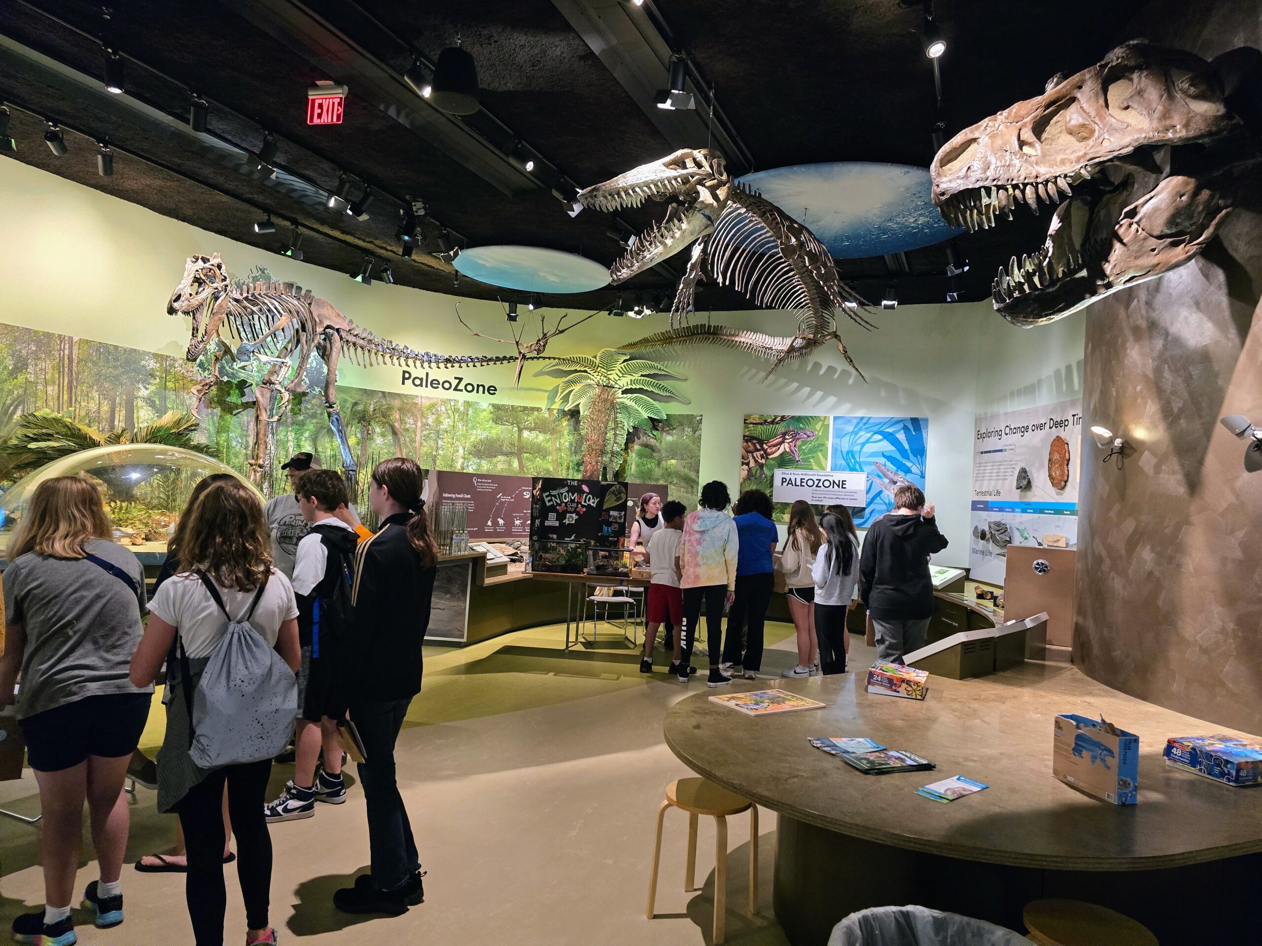 Visitors explore a museum exhibit featuring dinosaur skeletons and informational displays, with children engaging in activities at tables.