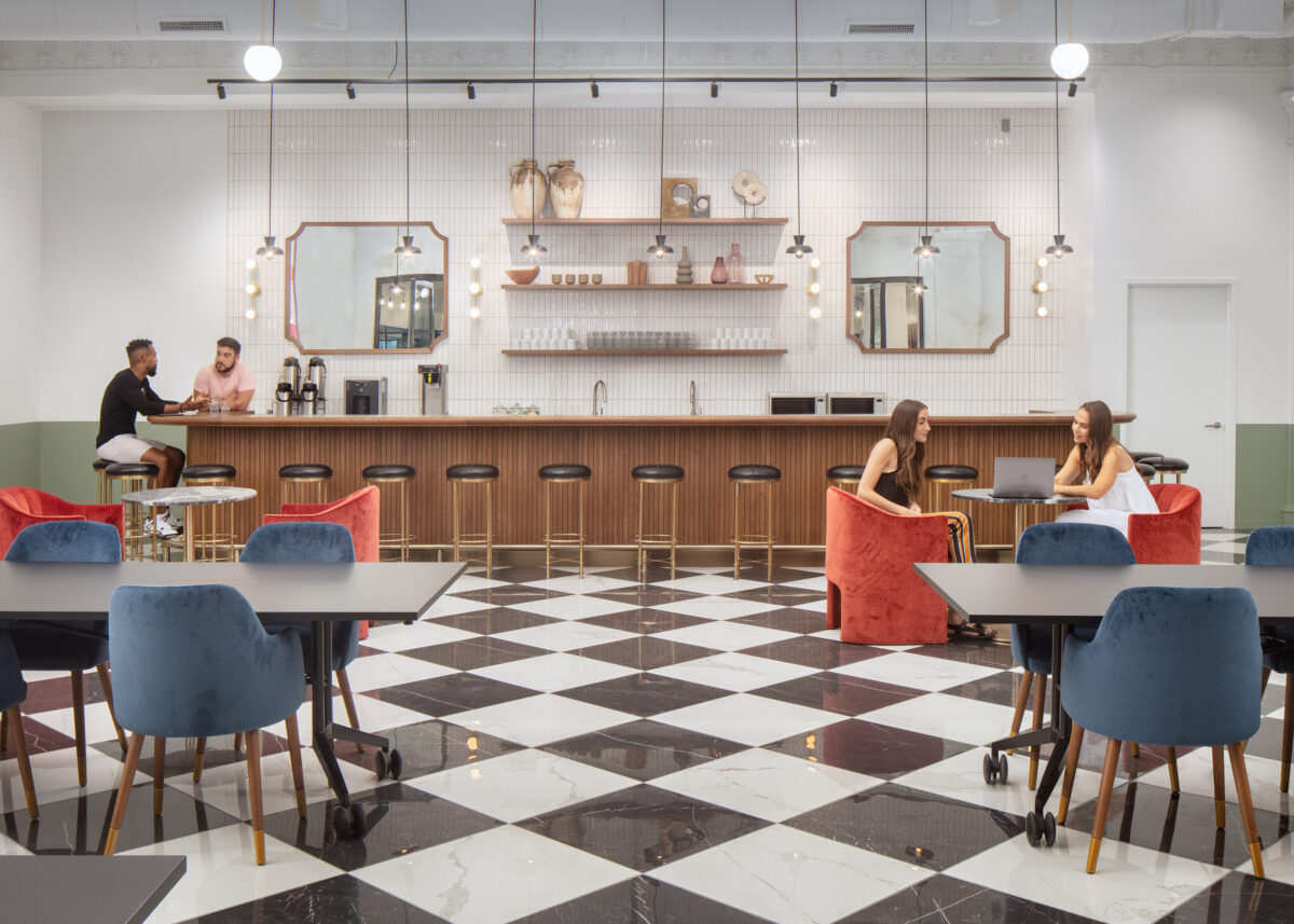 People seated at tables and bar counters in a coworking space with a black-and-white checkered floor and minimalist decor.