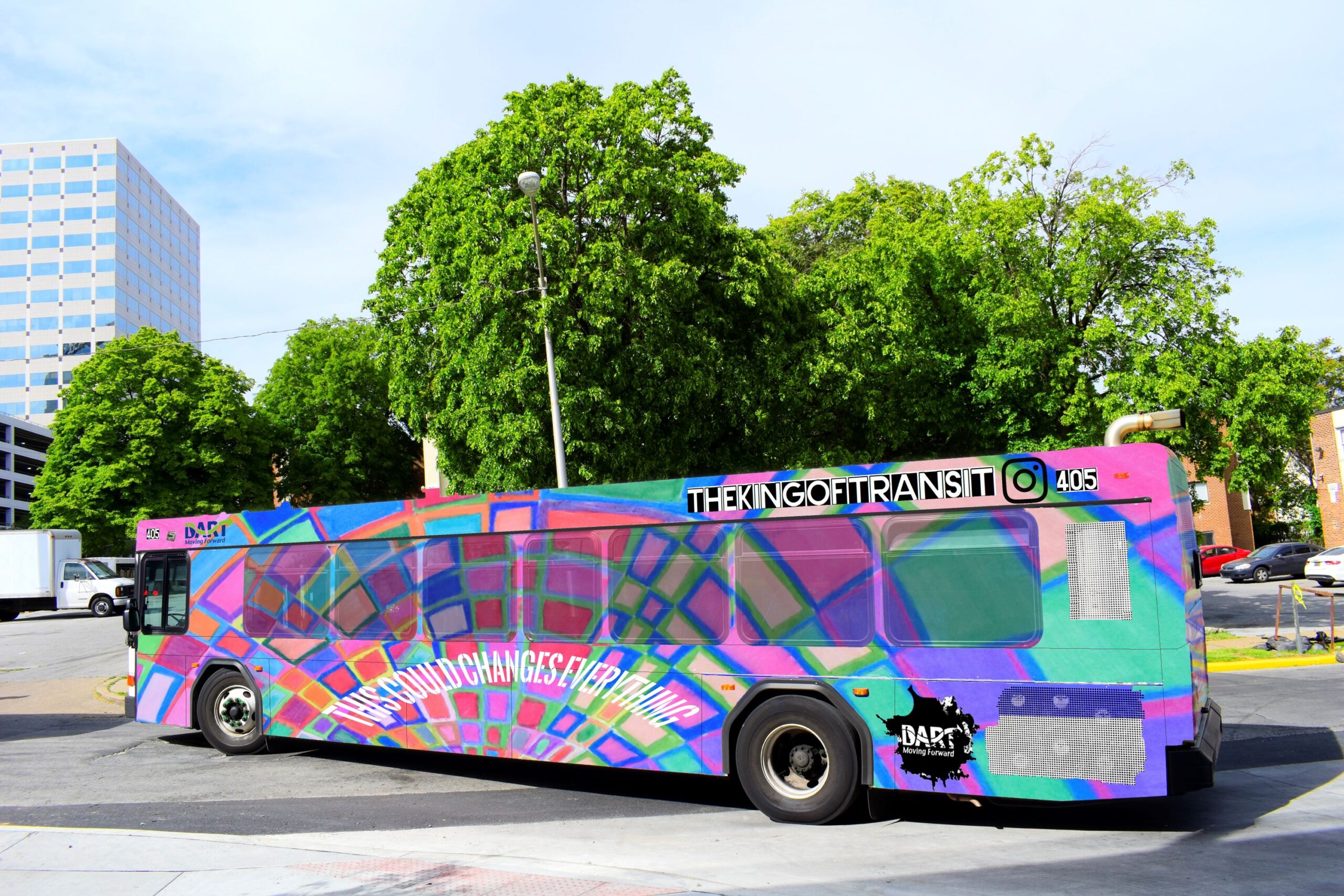 A colorful city bus with graffiti-style artwork and text reading "THE KING OF FIT TRANSIT" and "THE WORLD CHANGES EVERY 1/10 OF AN HOUR" is parked on a street.