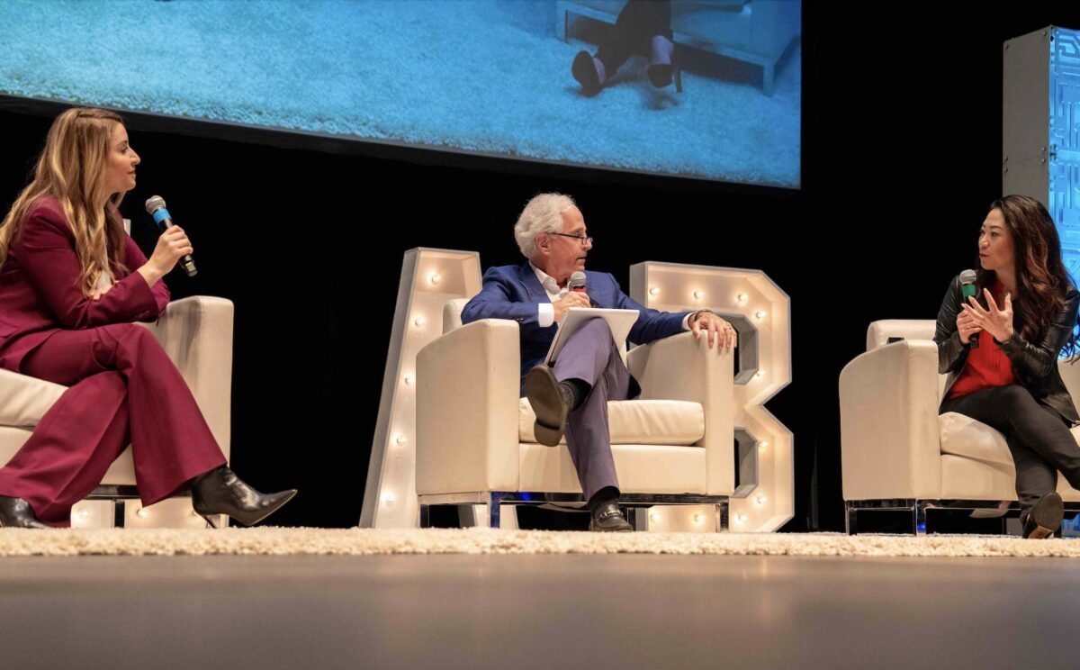 Three people on a theater stage in white chairs