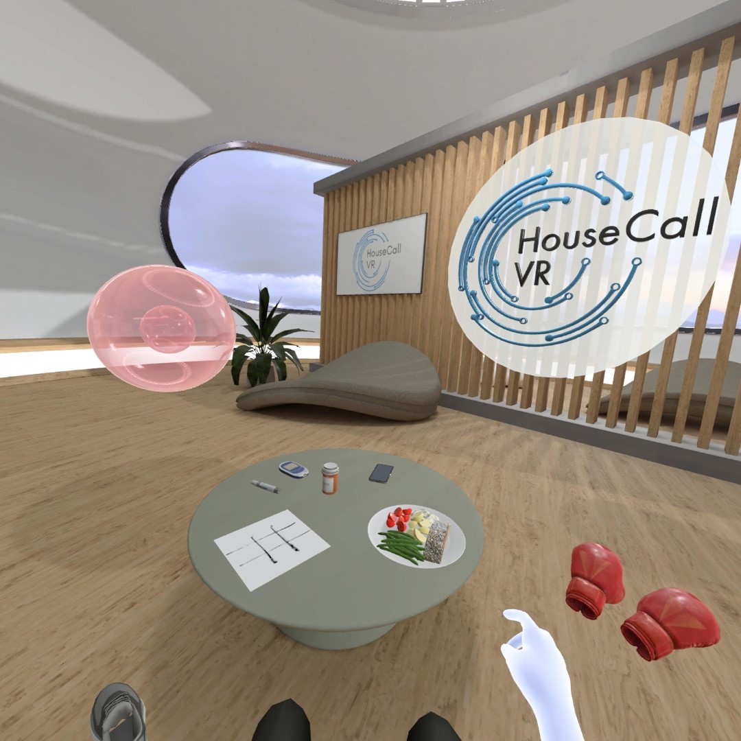 A virtual reality room with a round table displaying various objects. A sign on the wall reads "HouseCall VR." Chair and plant in the background.