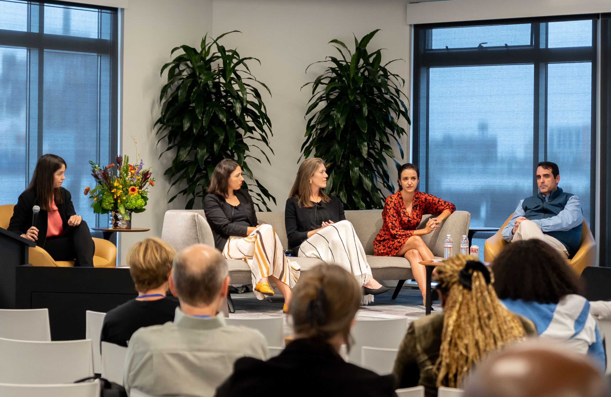 Four women and one man sit on brown chairs and a grey couch in front of an audience.