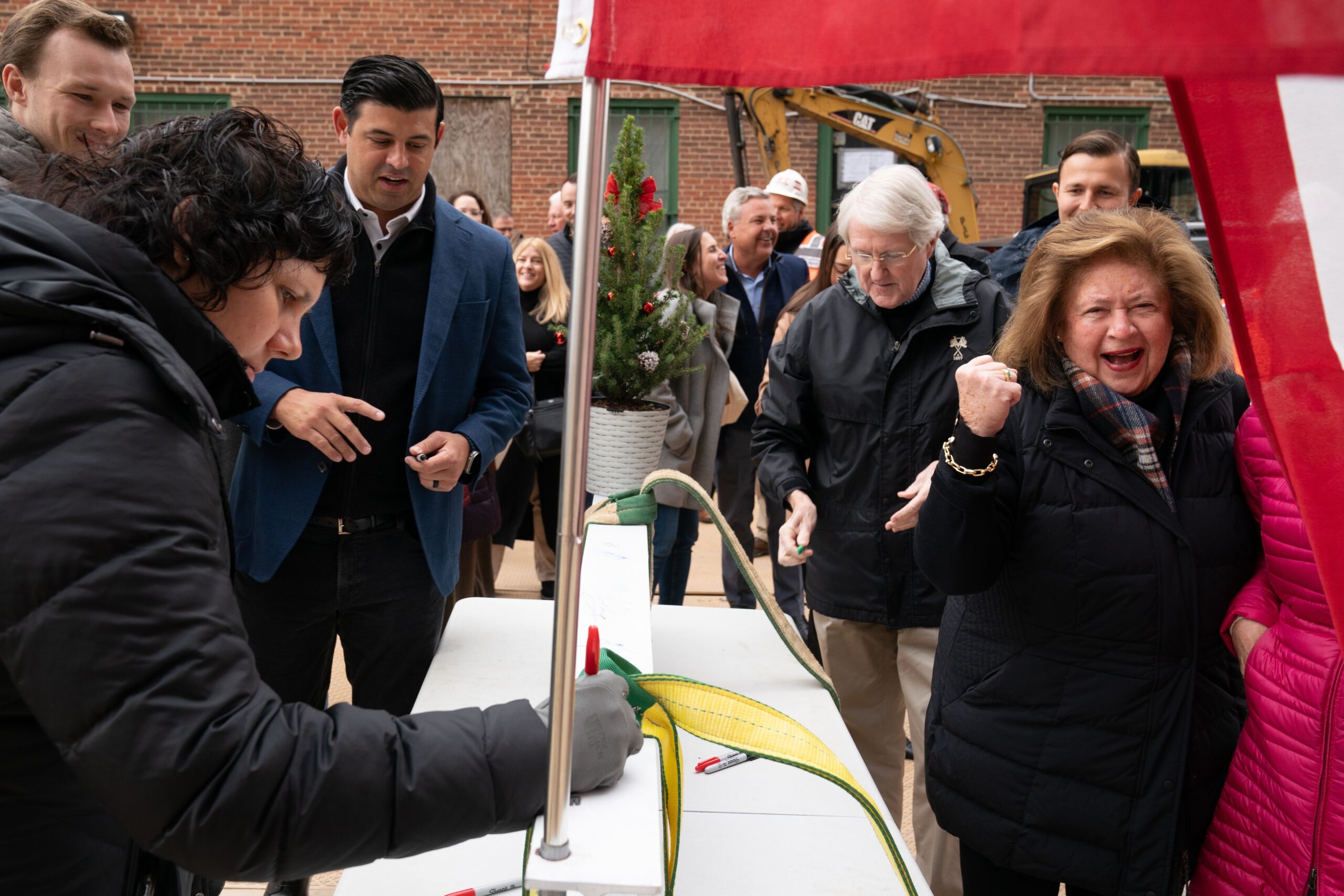 White woman smiles in black outfit near other people signing a steel beam. 