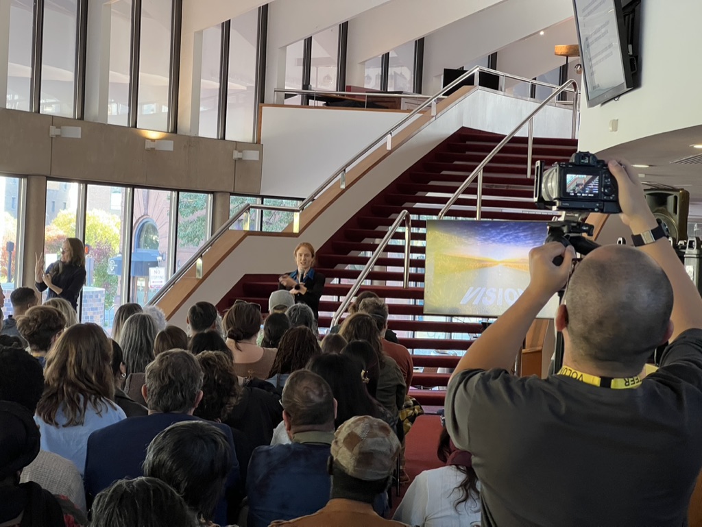 A crowd watches a red-haired woman in front of a red stairwell