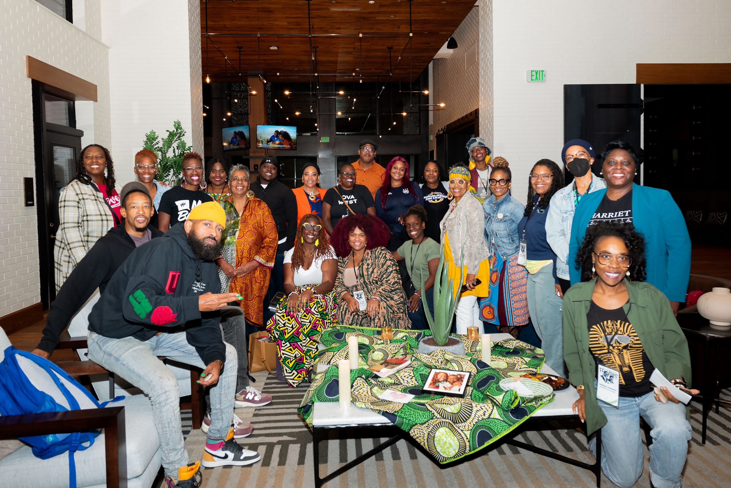 A group of Black people pose around a table in seated and standing positions in a room with white and black walls.