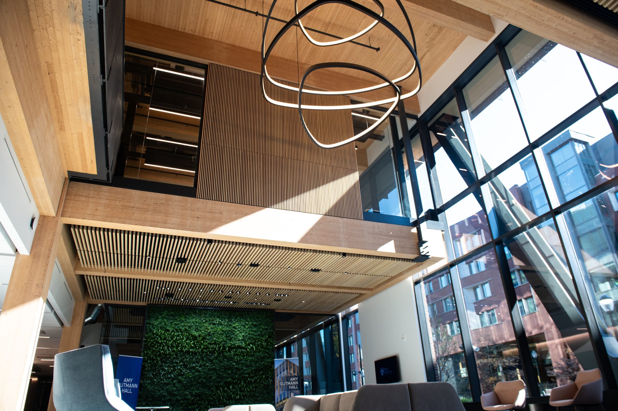 Modern interior with large glass windows, wooden beams, a green plant wall, and abstract circular light fixtures.