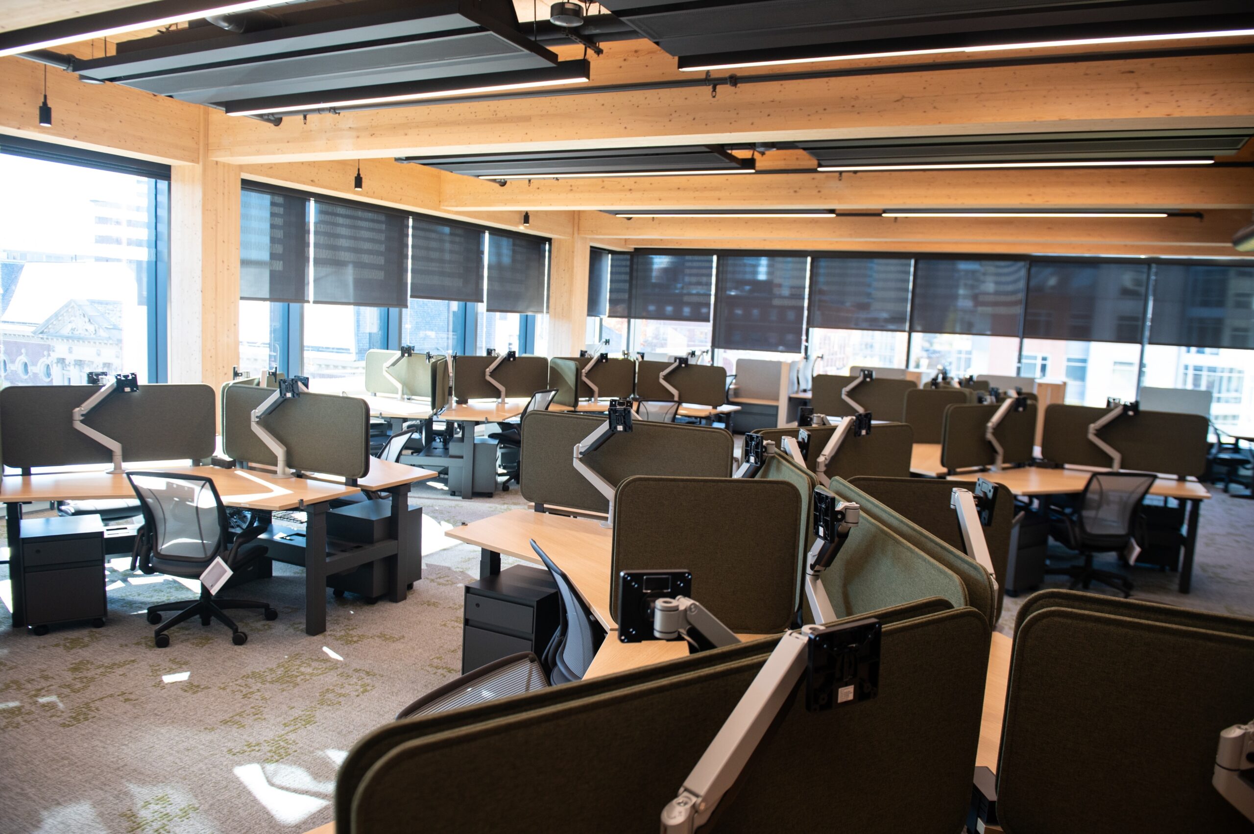 An empty open-plan office space with multiple workstations, chairs, and large windows.