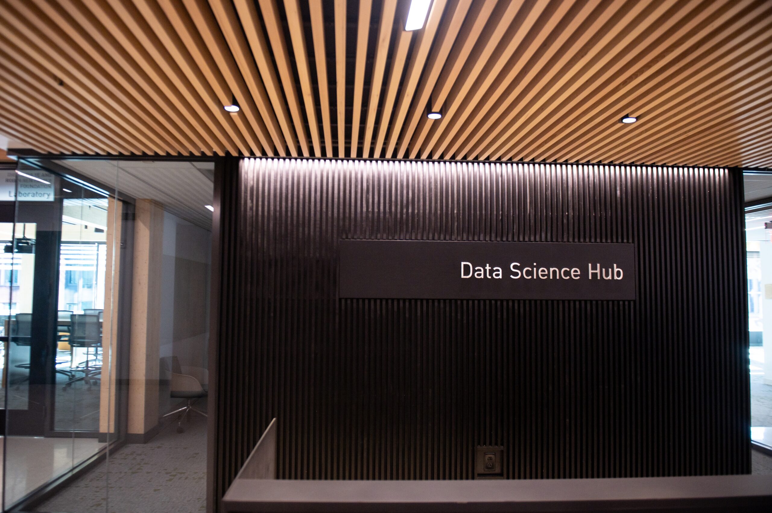 Entrance to the Data Science Hub with a modern, wood-slatted ceiling and a black wall featuring a sign.