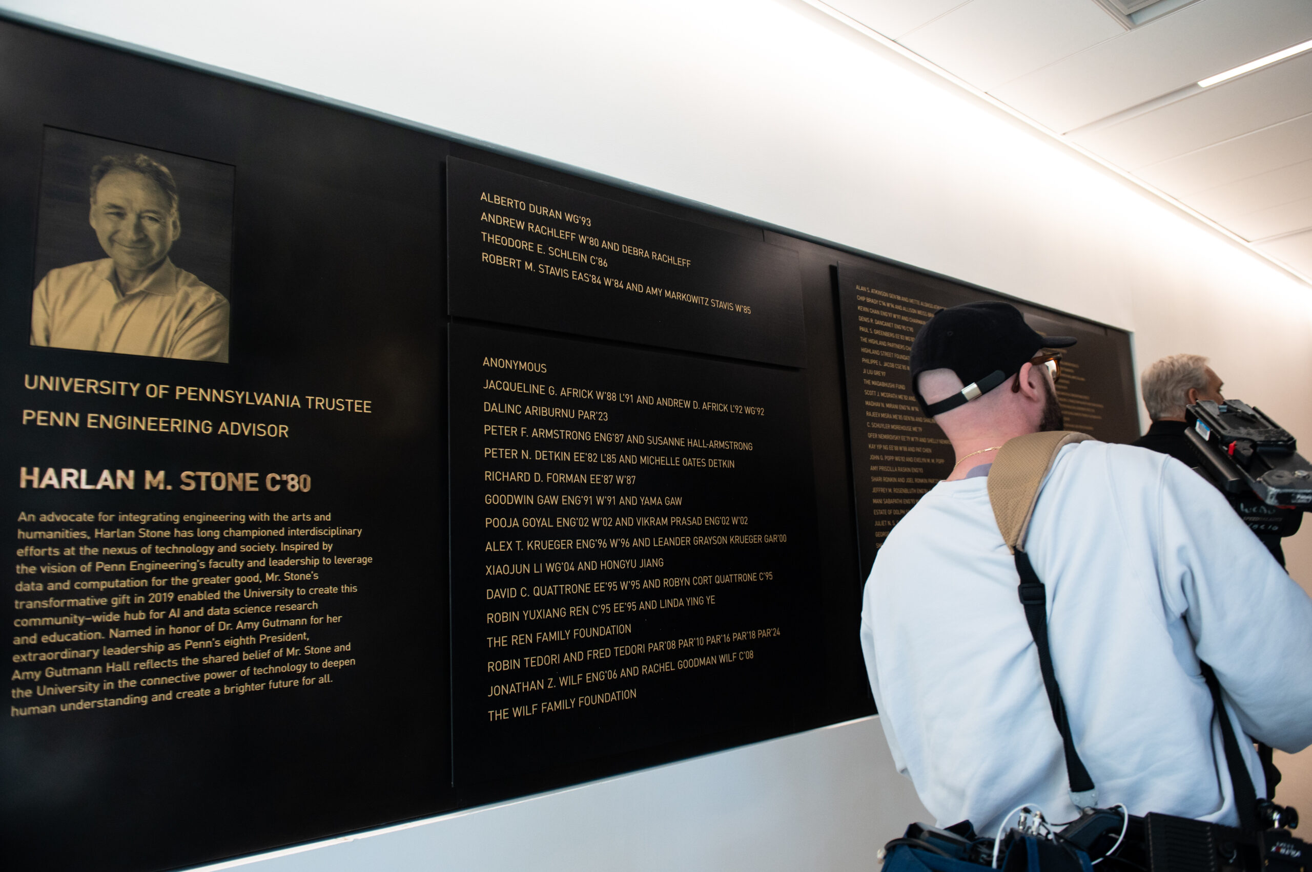 Two people read a wall displaying a dedication plaque and text about Harlan M. Stone, an alumnus and engineering advisor at the University of Pennsylvania.