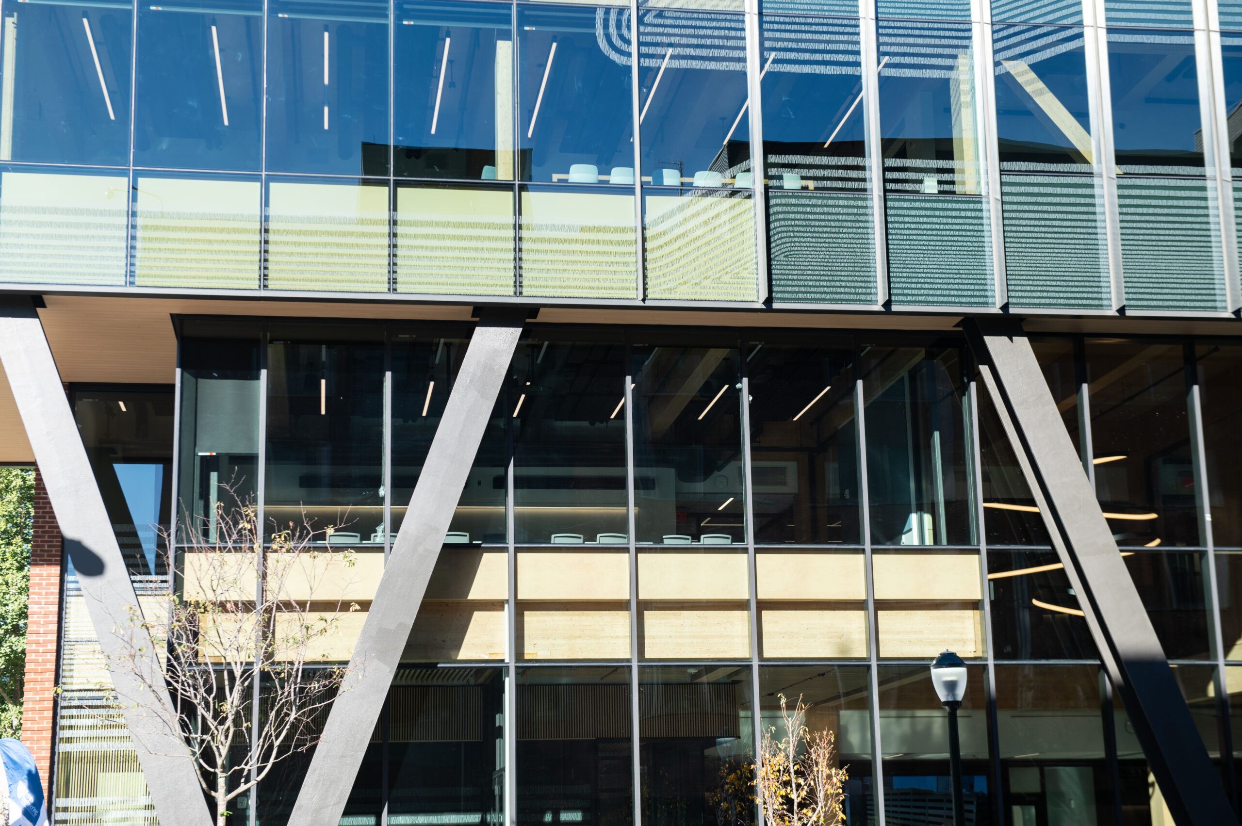 Modern building facade with large glass windows and V-shaped structural supports, seen on a sunny day.