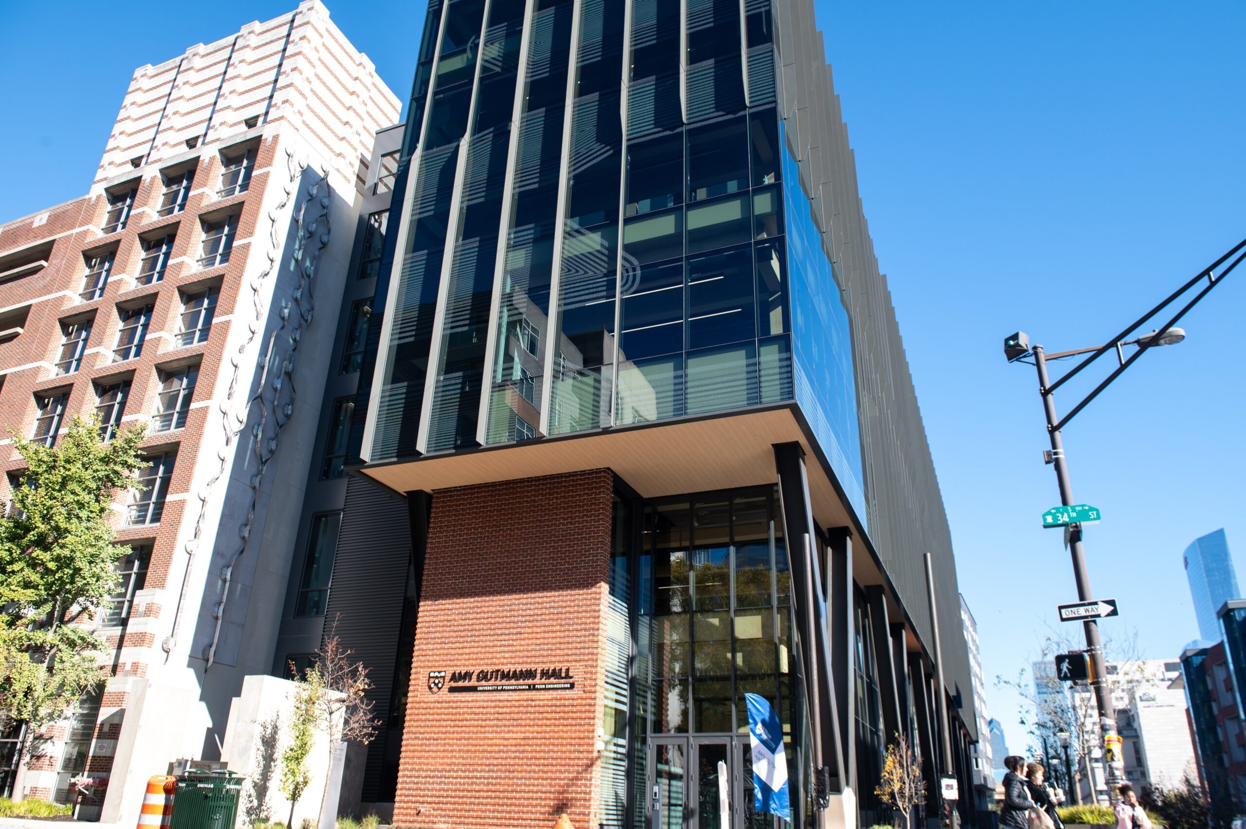 View of a modern multi-story building with glass and brick facade, located at a street corner under a clear blue sky.