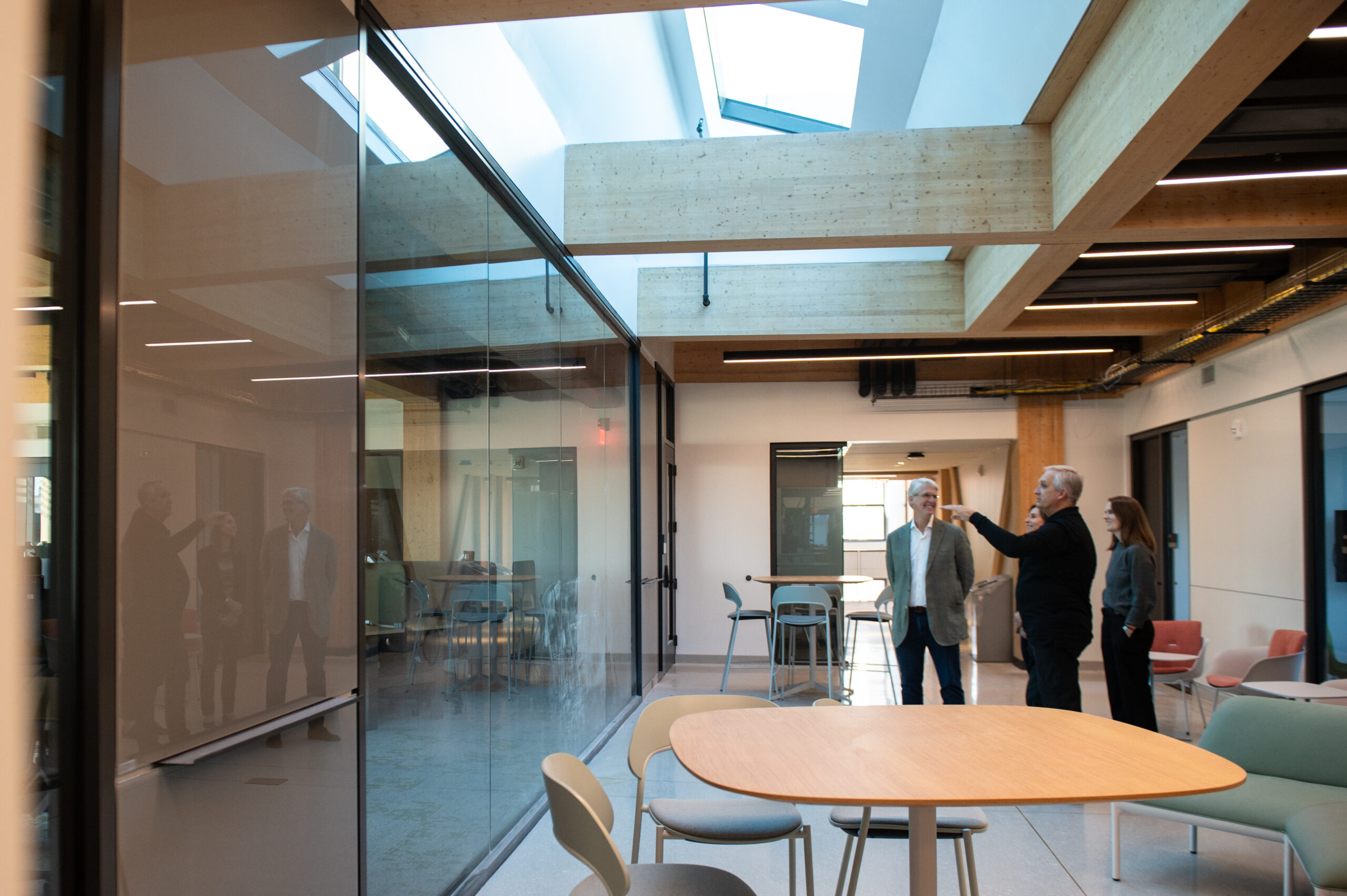 Four people stand inside a modern office space with wooden beams and glass walls, looking in different directions.