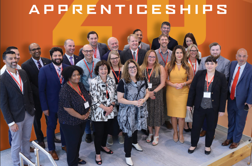 Over 20 people stand together for a photo. The word 'Apprenticeships' above their heads. 