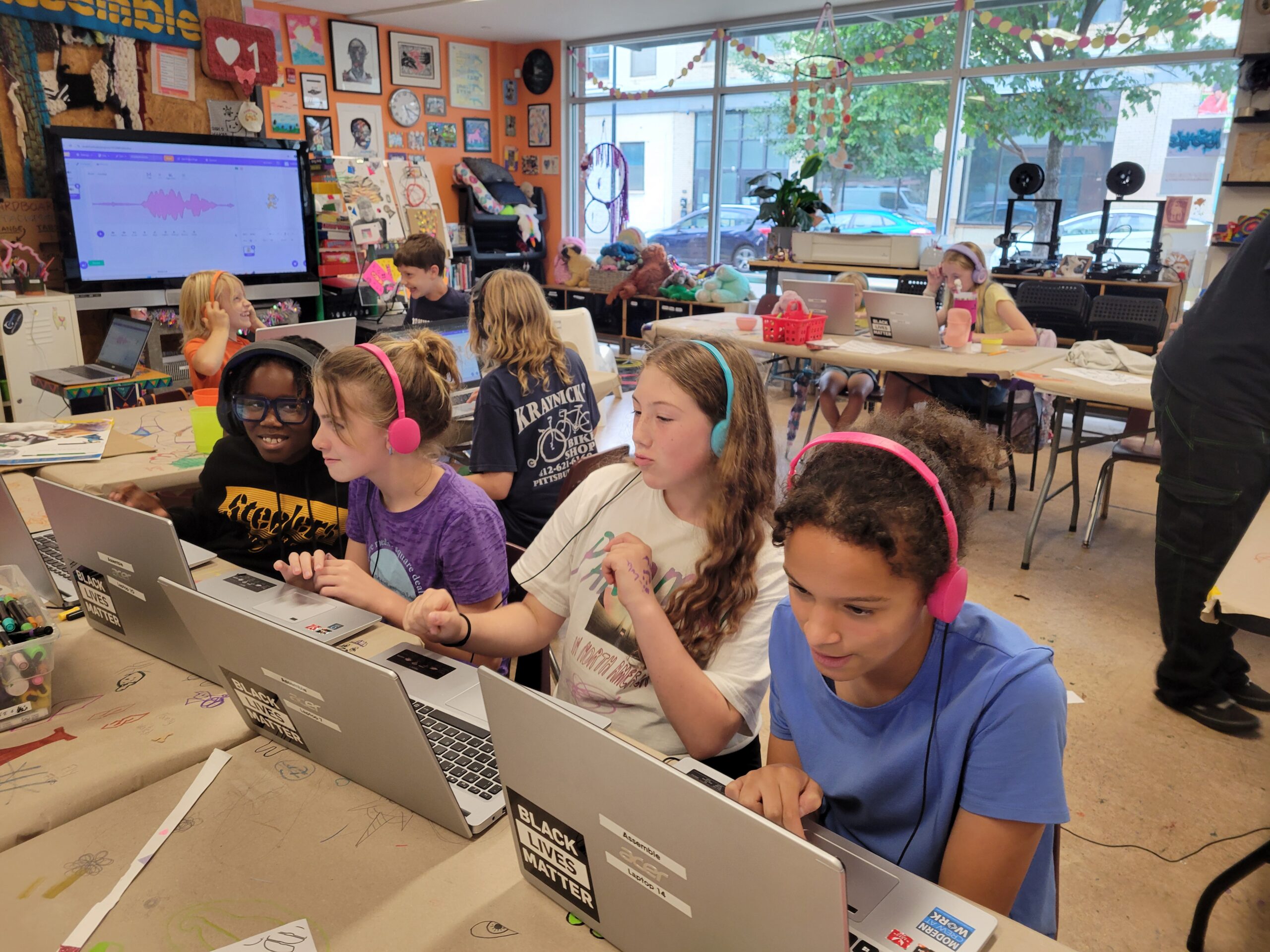 Students sit at desks with headphones and laptops. 