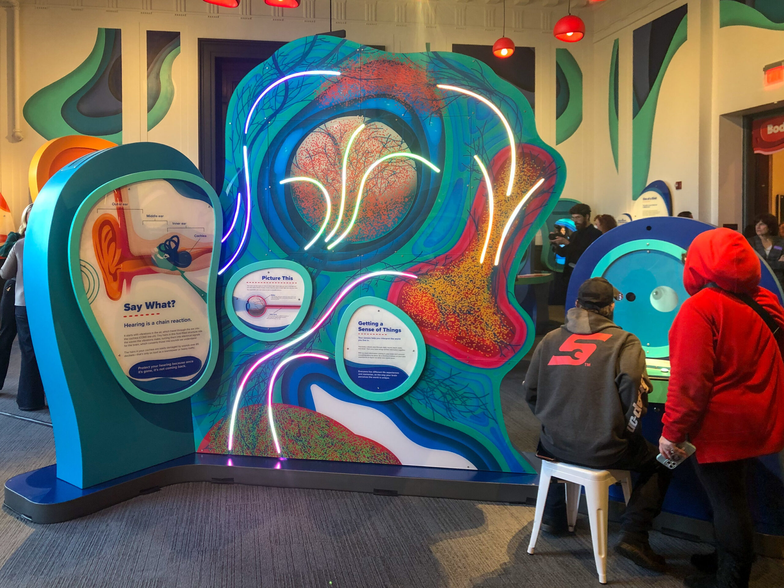 People interact with colorful, abstract art displays in a modern exhibit space.