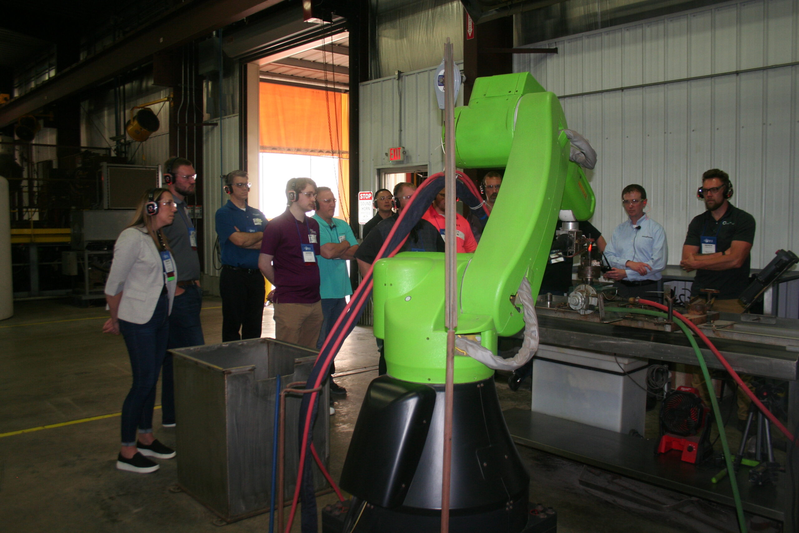 People observing a green robotic arm demonstration in an industrial setting.